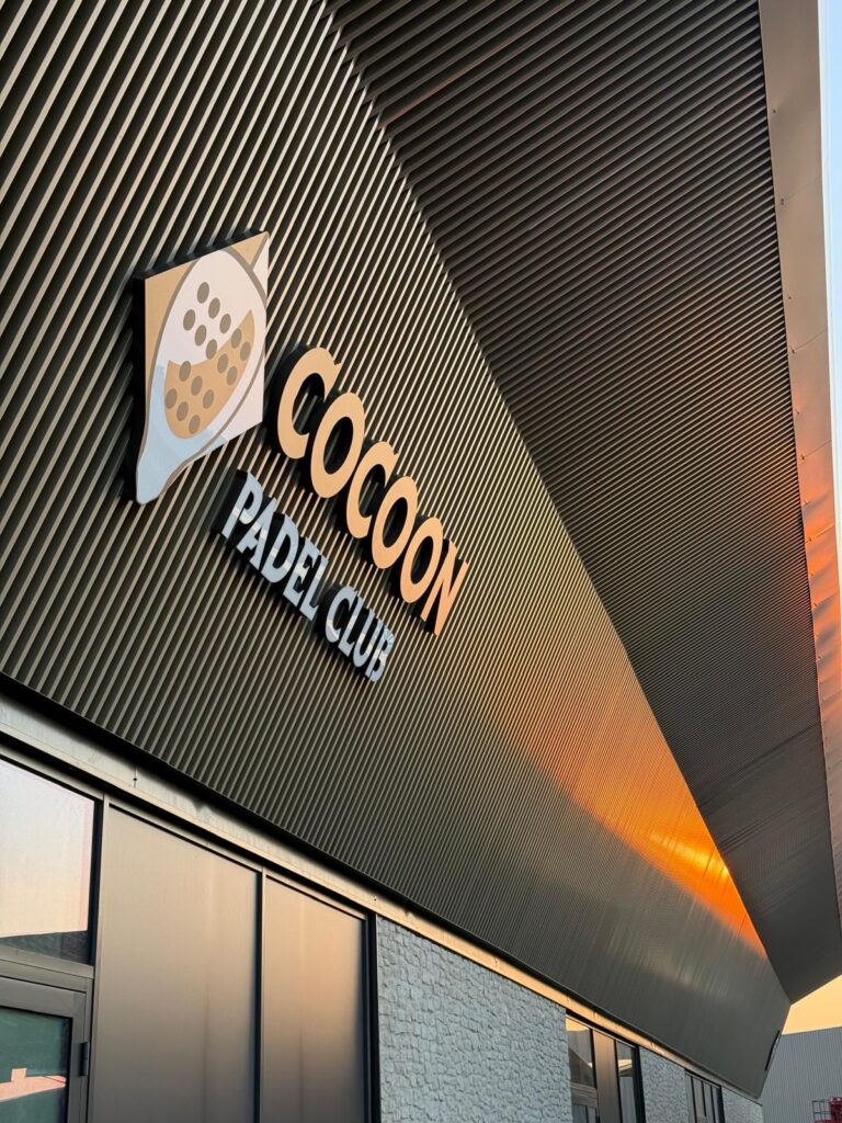 Enseigne extérieure du Cocoon Padel Club éclairée par le soleil couchant, Saint-Aubin-Celloville