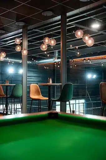 Coin lounge avec billard et tabourets surplombant les terrains de padel indoor