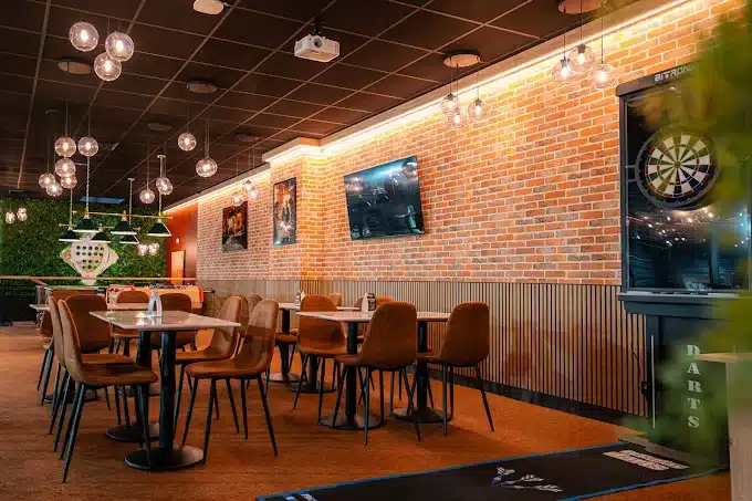 Espace bar-restaurant avec tables, coin flechettes et ecrans au Cocoon Padel Club Rouen