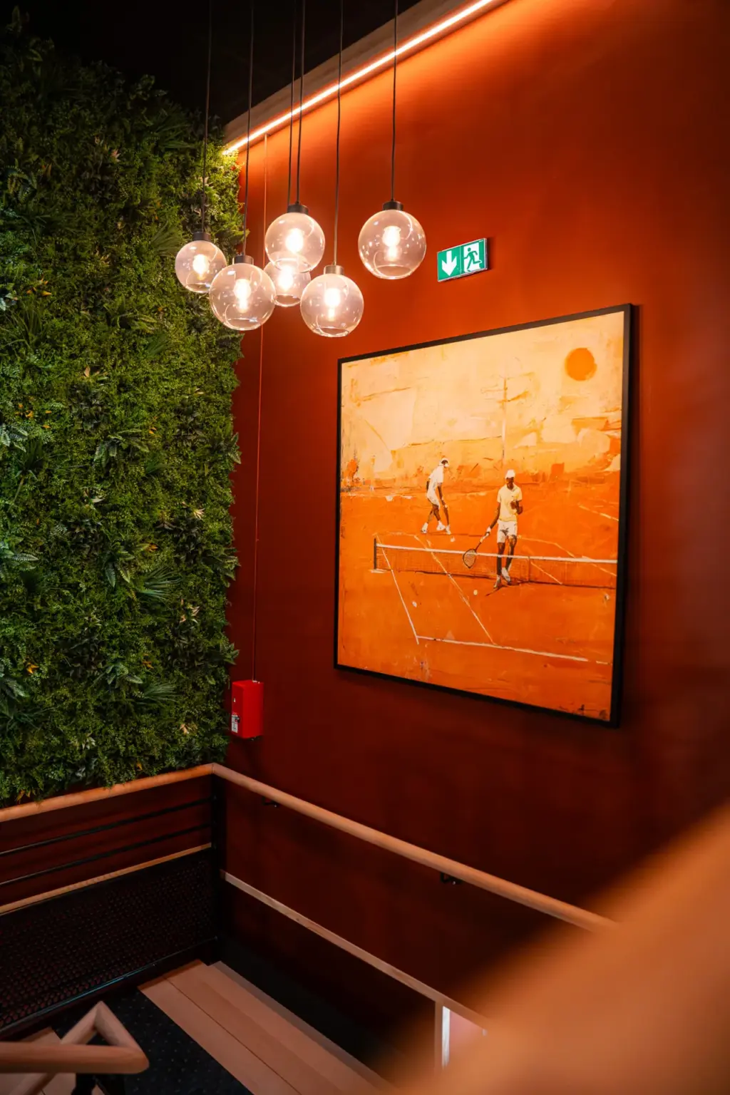 Suspensions lumineuses, tableau terre battue et mur végétal dans l'espace intérieur du club de padel