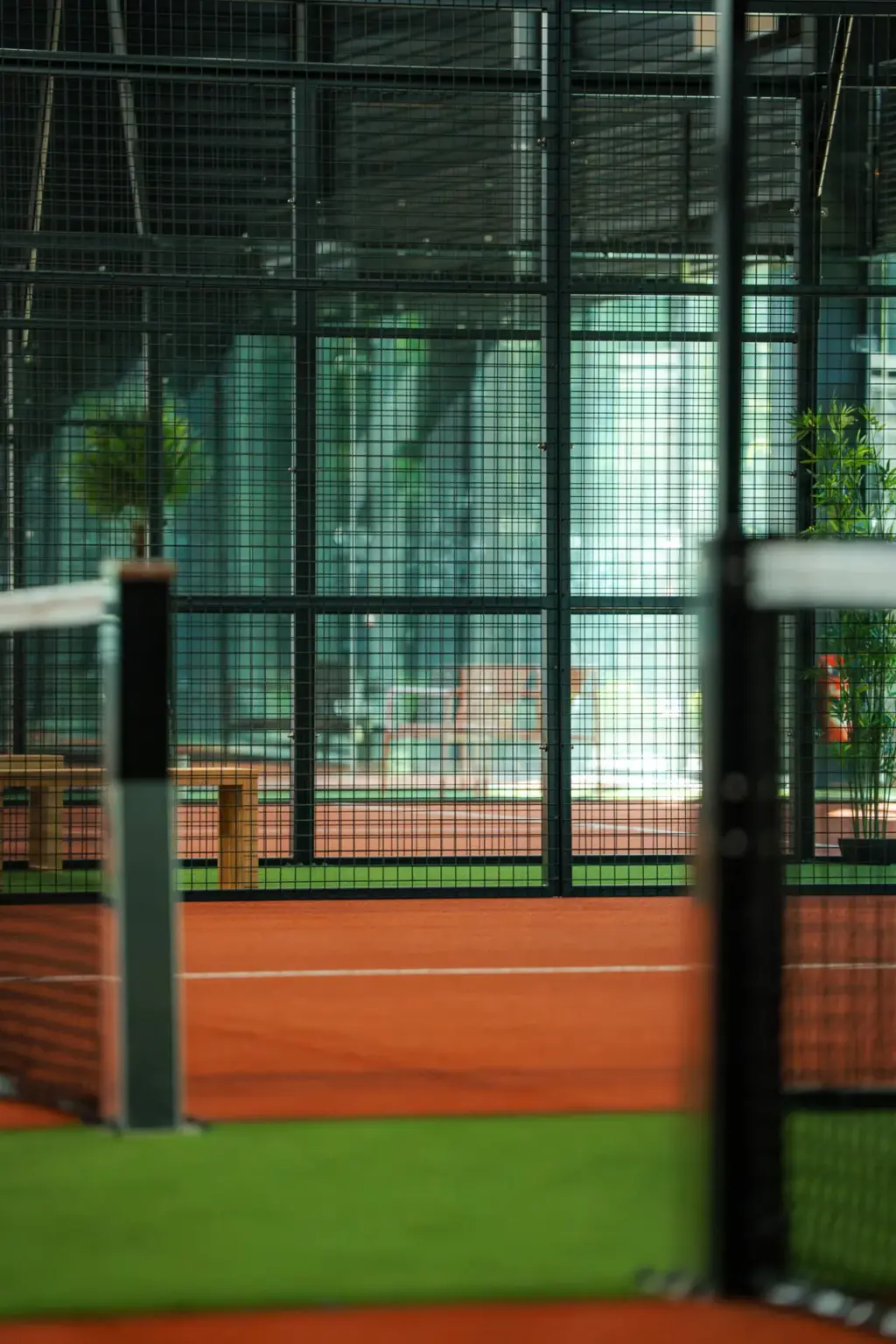 Court de padel indoor en terre battue derrière la paroi grillagée végétalisée, Cocoon Padel Club Rouen