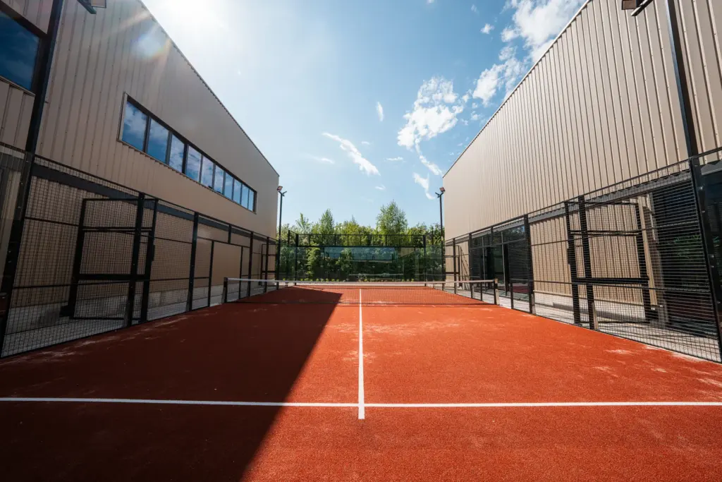 Court de padel extérieur ensoleillé encadré par les halles du club près de Rouen