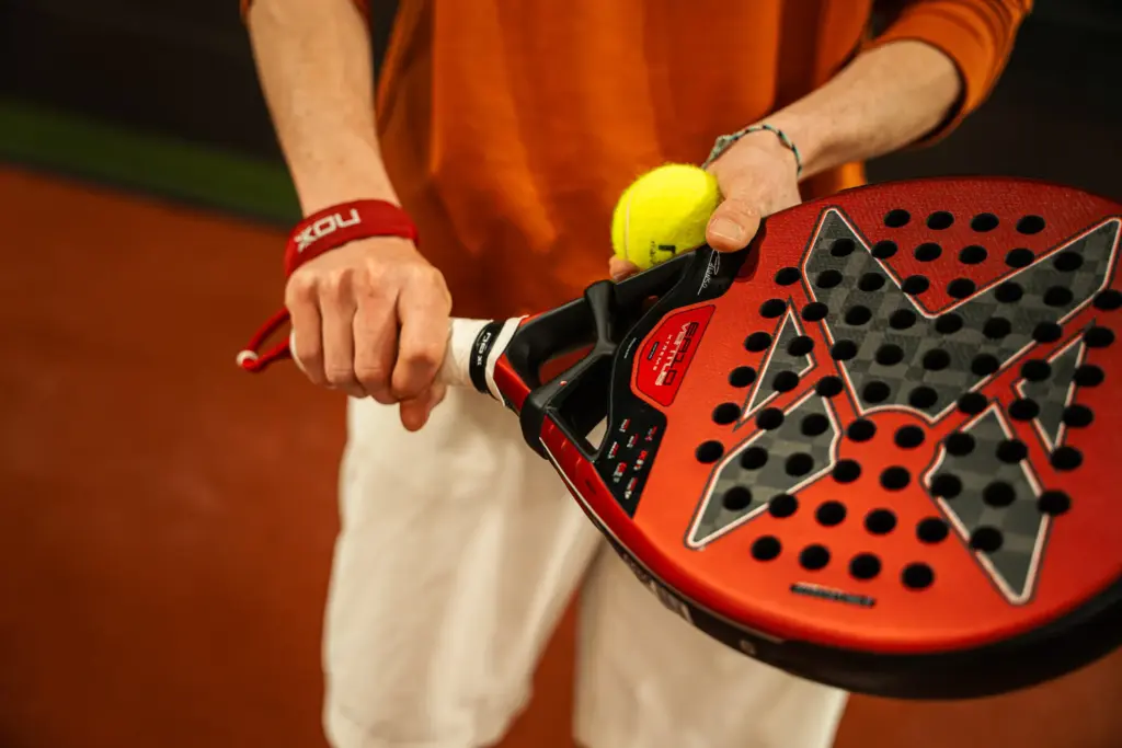 Joueur tient une raquette de padel NOX rouge et une balle jaune sur le terrain, Cocoon Padel Club à Rouen