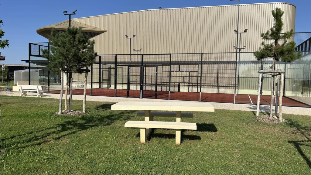 Table de pique-nique en pierre sur la pelouse arborée face aux terrains extérieurs du Cocoon Padel Club
